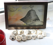 collection of small stones with faces and figures drawn on them in front of a small framed painting
