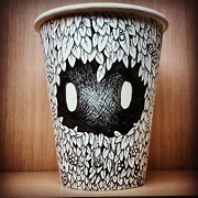 paper cup with two eyes peering out from a forest of leaves drawn on it